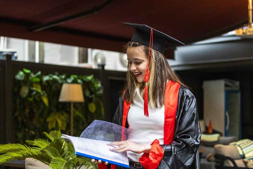 young student wearing graduation cape looking her notebook